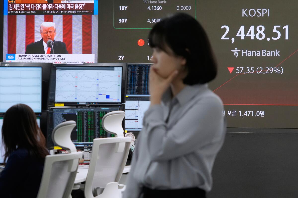 A currency trader at a bank in Seoul with President Trump visible on a TV screen.