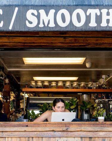 A person sits in an open window, working on a laptop, at the Cow's End restaurant