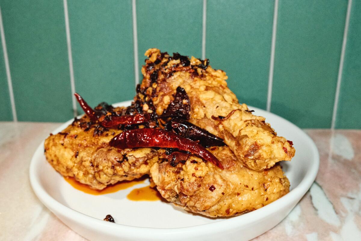 A white dish of Firstborn's signature Chongqing-inspired fried chicken on pink marble against a green tile wall