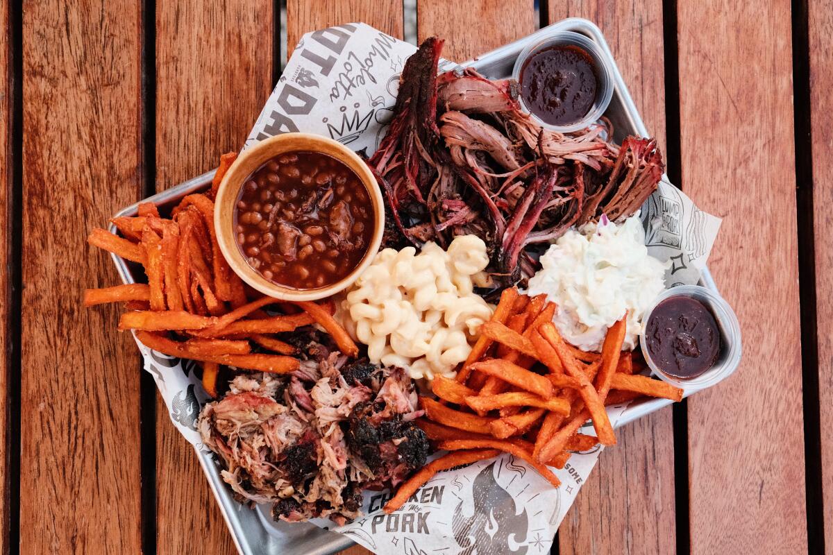 A tray of shredded brisket, pulled pork, brisket baked beans, coleslaw, sweet potato fries and mac and cheese on a wood table