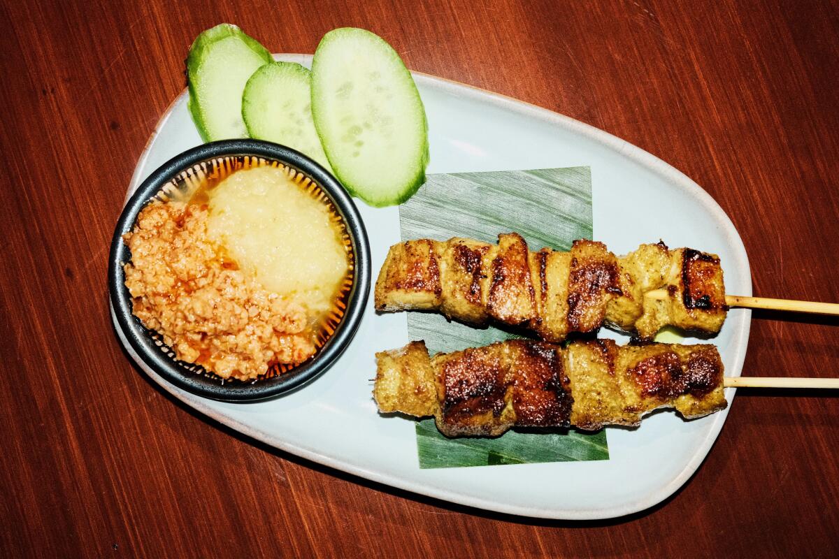 Two skewers of chicken satay with cucumber and dipping sauce at Rasarumah restaurant.