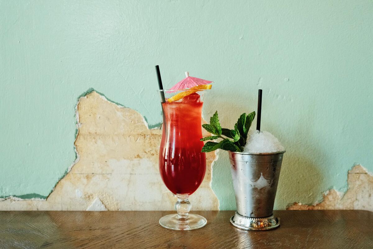 A hurricane and a mint julep (right) against a cracked light green wall at Evangeline Swamp Room in Chinatown