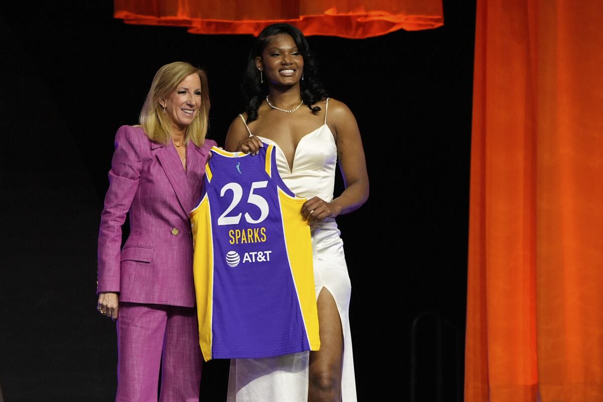 A woman in a pink pantsuit, left, and another in a white dress hold a purple-and-yellow 25 Sparks jersey