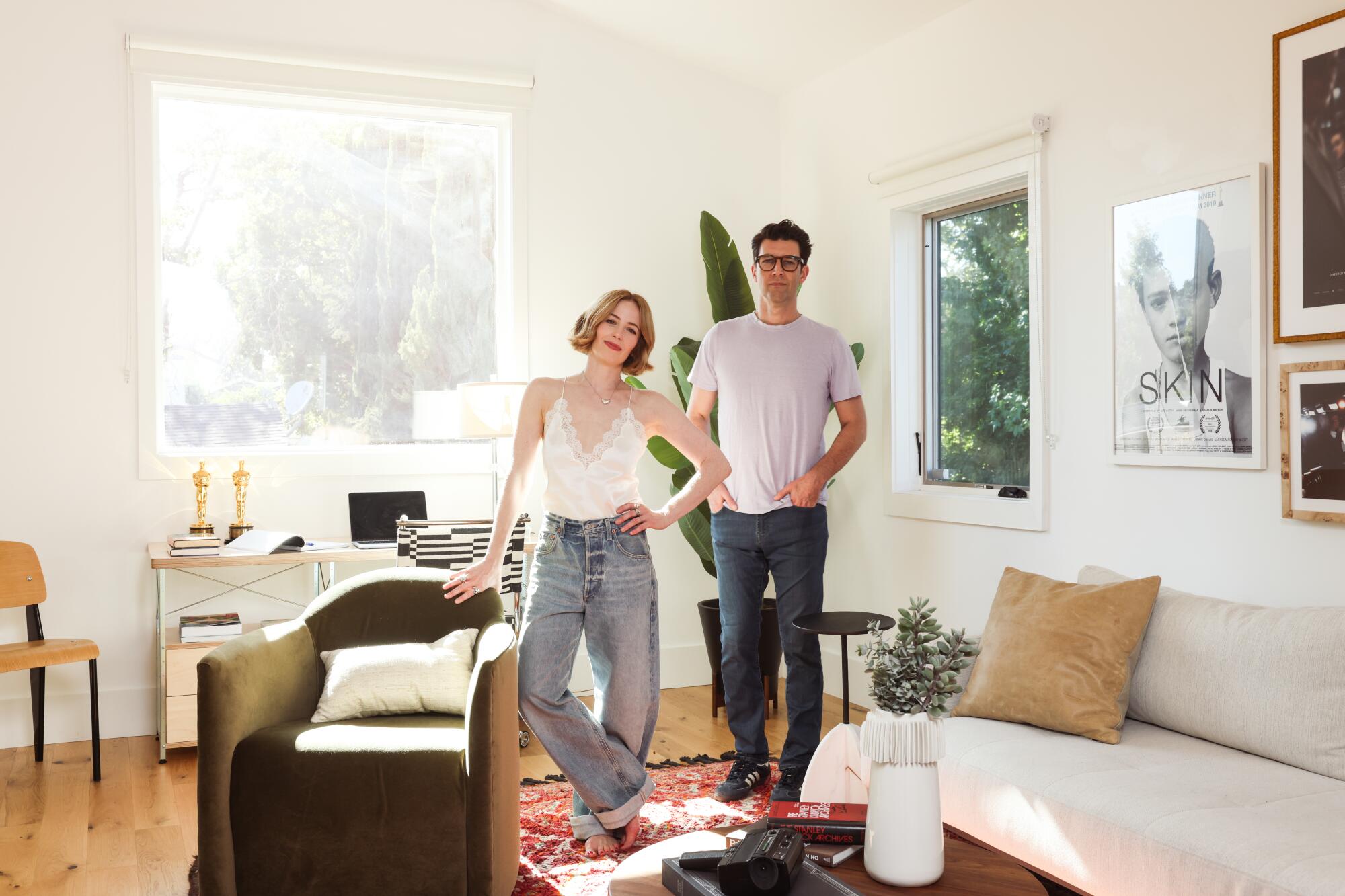 A woman and a man, casually dressed, stand in a sunny living room