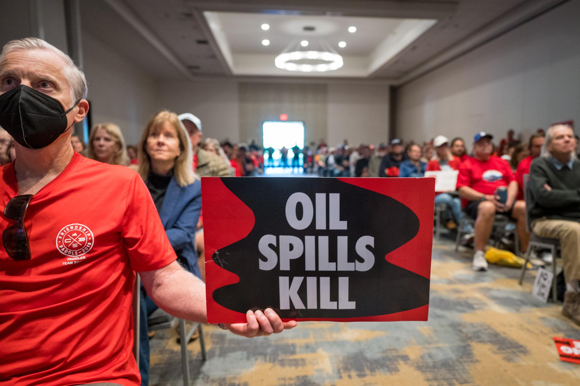 A man in a red T-shirt holds a sign that reads "Oil spills kill."