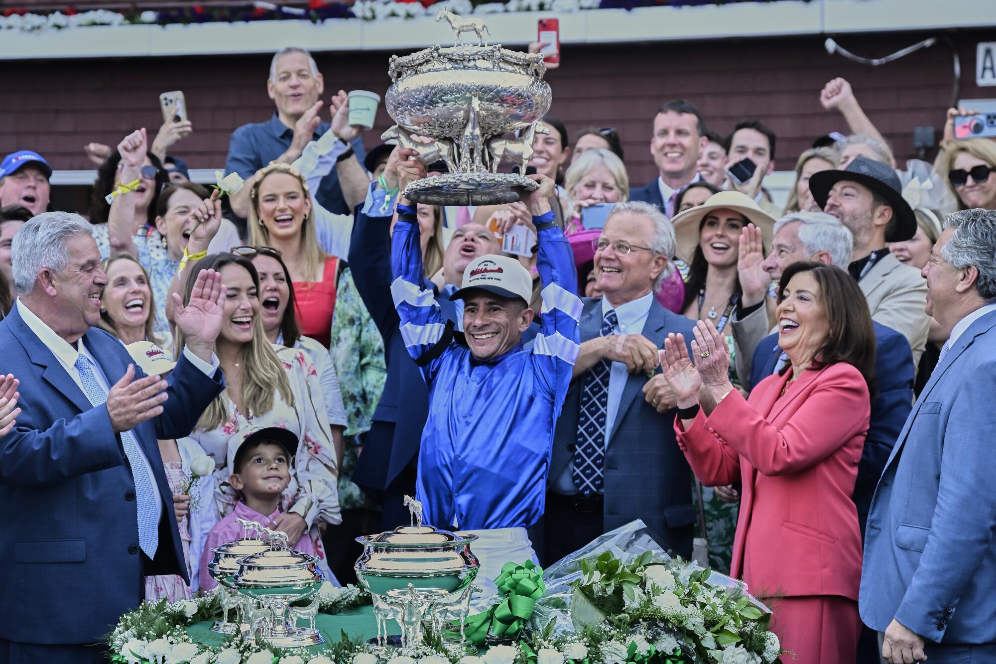Jockey Junior Alvarado, center, holds up the August Belmont Trophy after riding Sovereignty to victory in the Belmont Stakes.