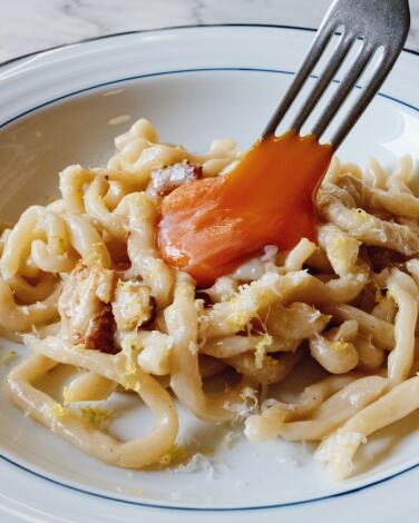 A fork dips into a whole egg yolk atop smoked-eel carbonara at Buvons Wine Bar + Restaurant in Long Beach.