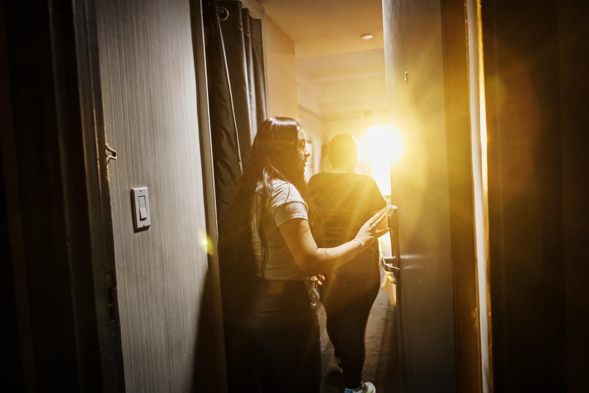 A girl and a woman walk into a room as sunlight blasts through a window.