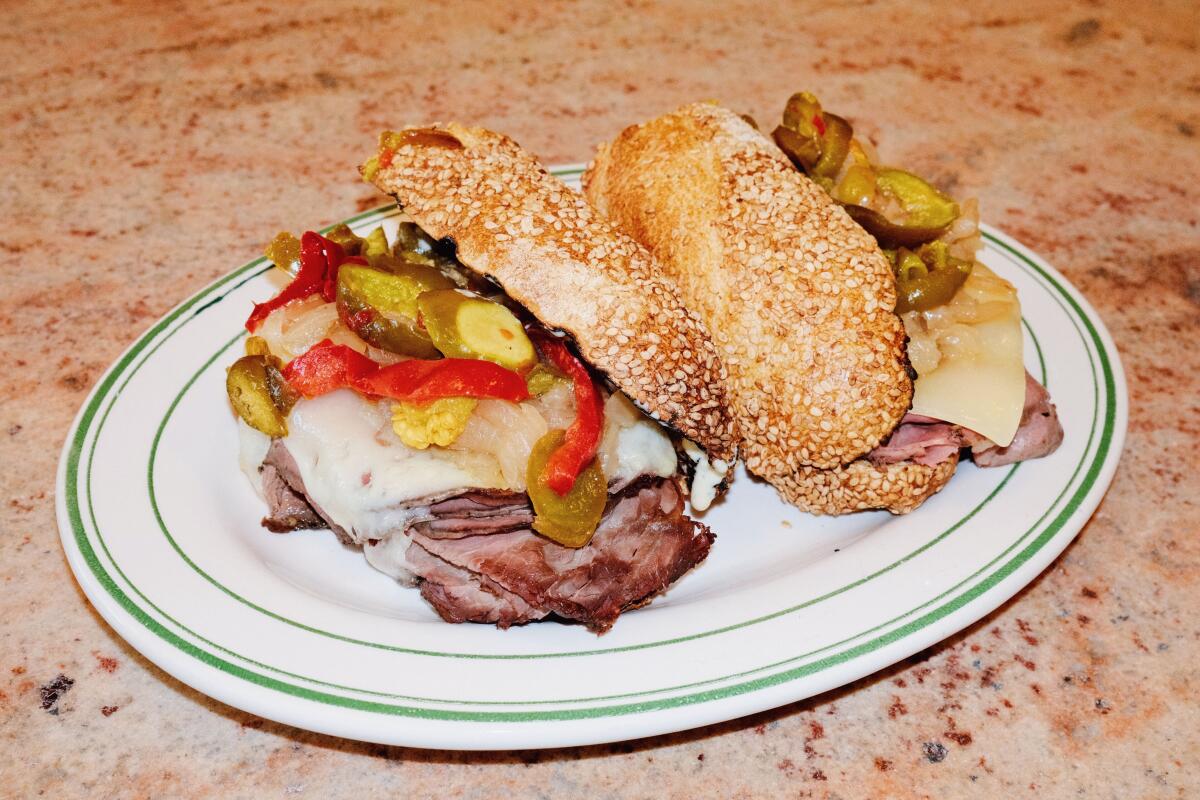 Two halves of a packed roast beef and peppers sandwich on sesame bread on a white plate
