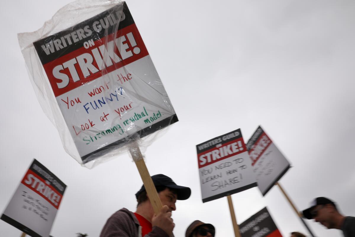 A WGA supporter walks with a sign that reads, "You want the funny? Look at your streaming residual model."