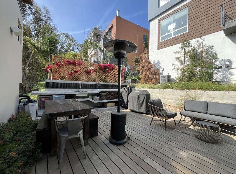 A deck with an outdoor kitchen, barbecue, mini fridge and table