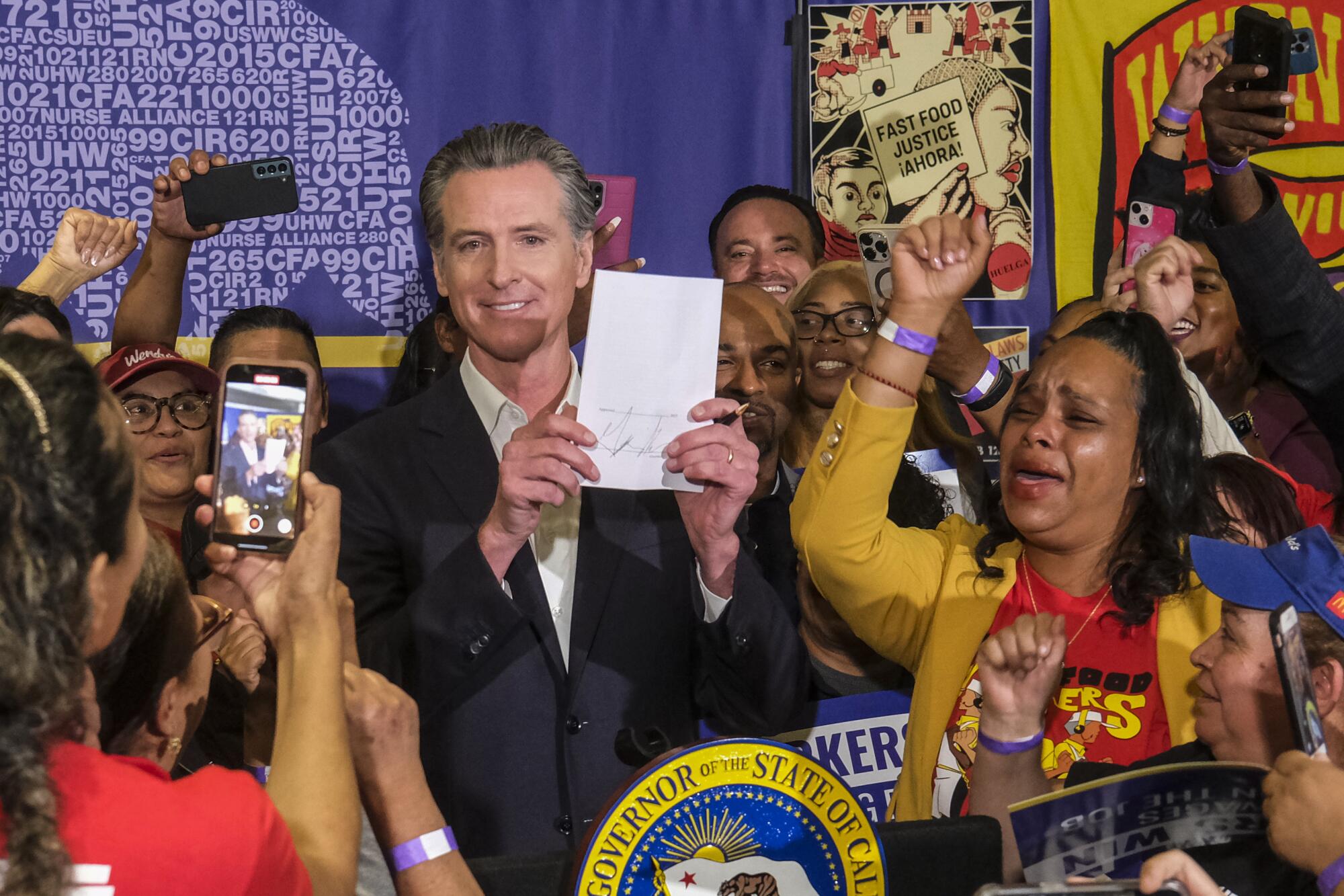 California Gov. Gavin Newsom, surrounded by cheering people, holds up a sign.
