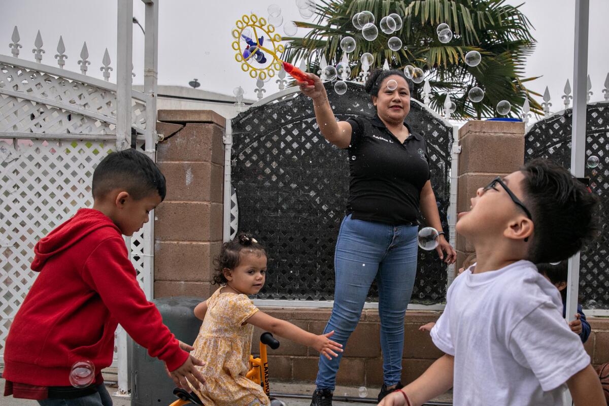 A woman waves a bubble wand for young children.