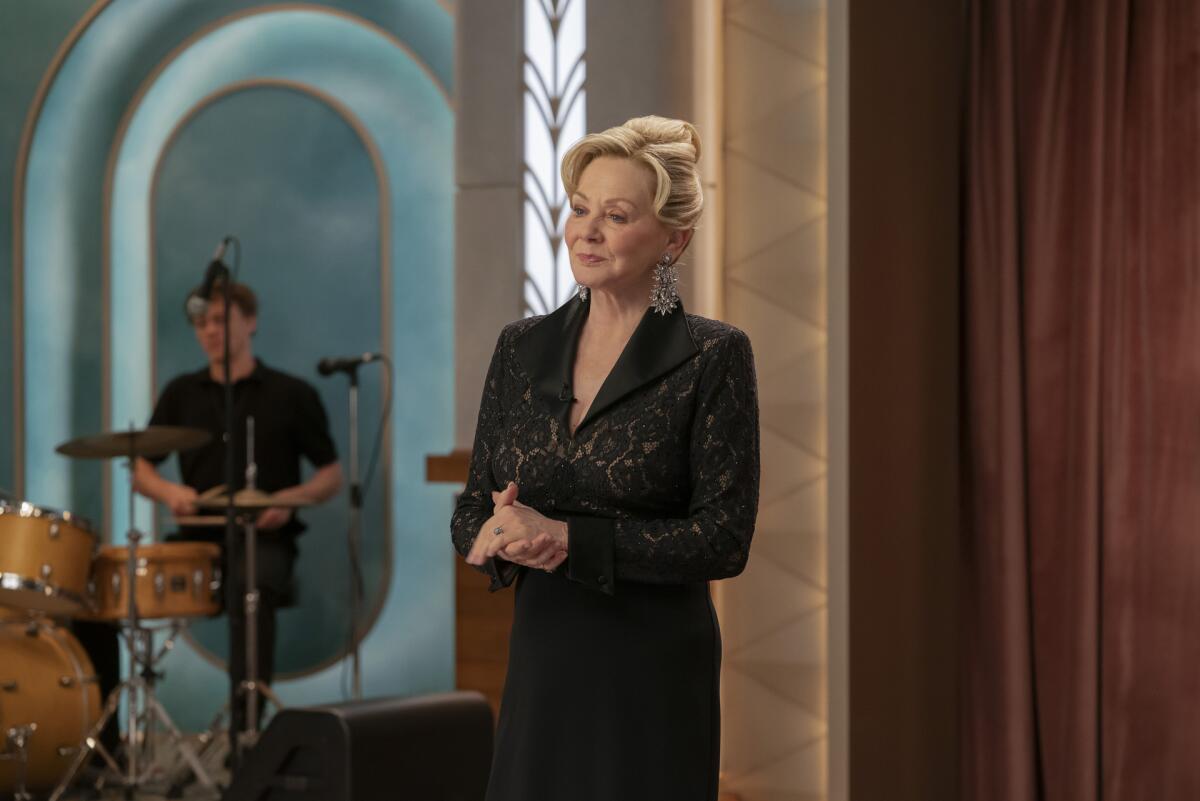 A blond woman whose hair is in an updo wearing a black long-sleeve lace dress.