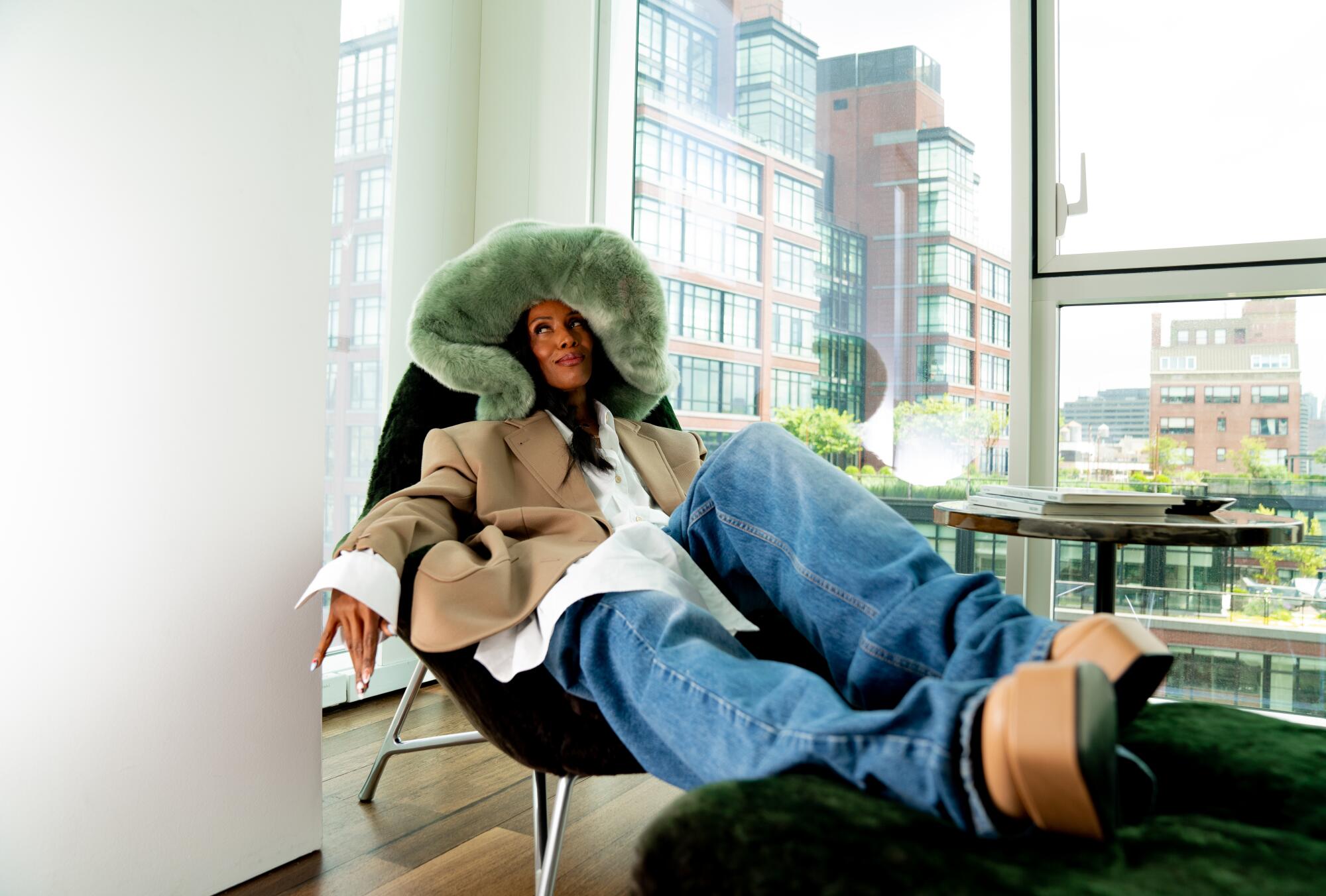 June Ambrose sits on a chair, wearing a large, soft green hat.