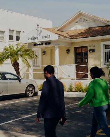 Two people walk in the parking spaces in front of Healing Hands Wellness Center in a small yellow building