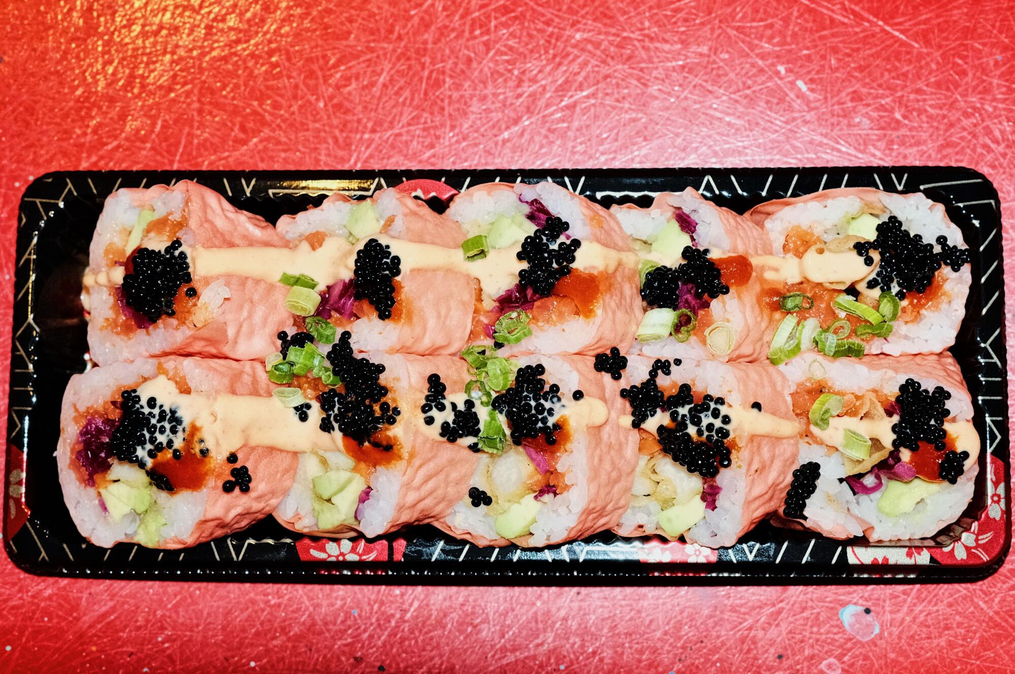 An overhead photo of the Barbie Roll sushi in a to-go container on a red background.