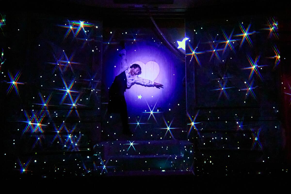 An actor caught mid-pose in a starry landscape with a heart at its center.