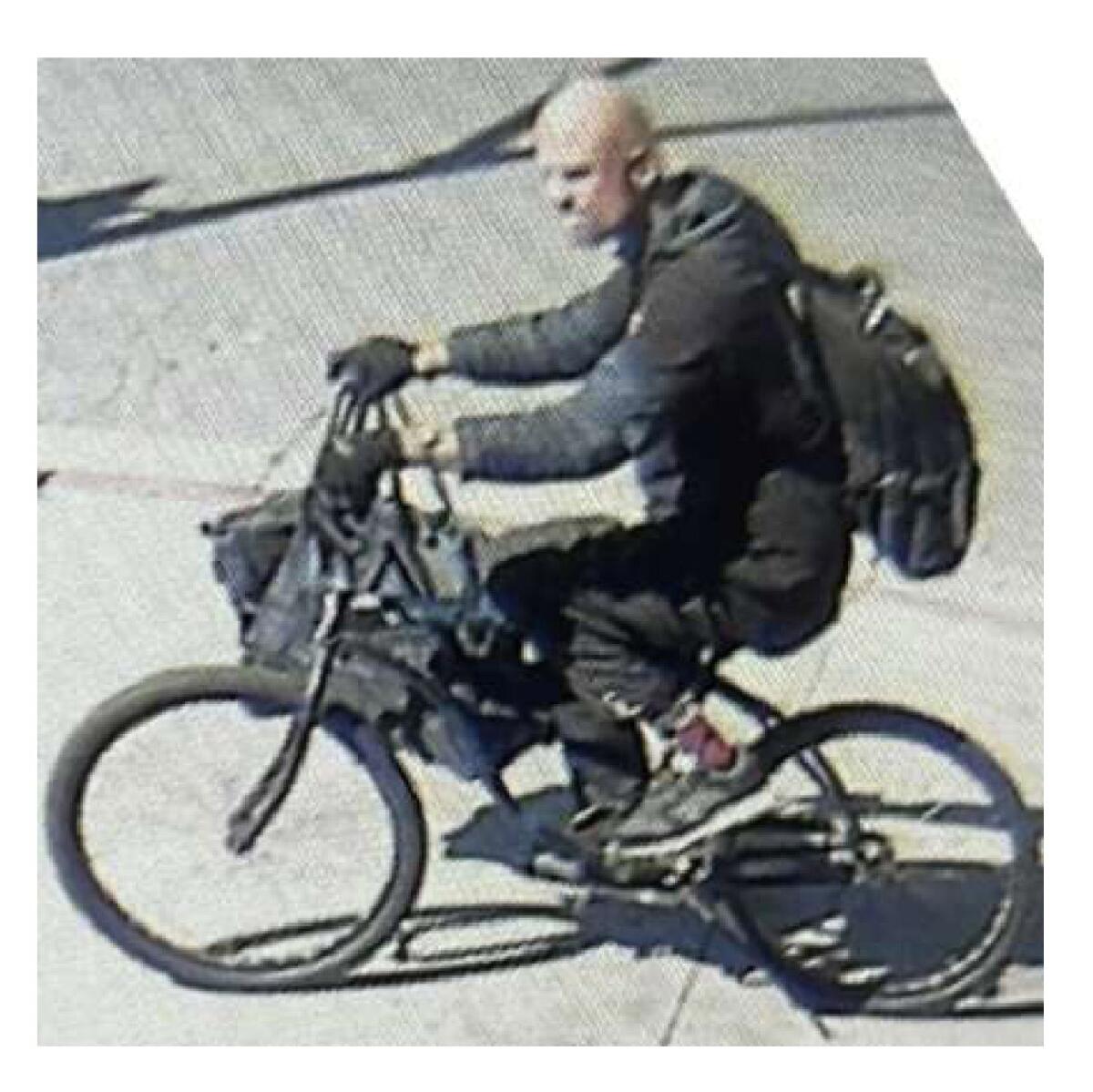 A man dressed in black rides a bicycle and carries a duffel bag.